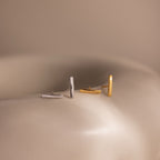 Two pairs of bar stud earrings, one silver and one gold, on a neutral background