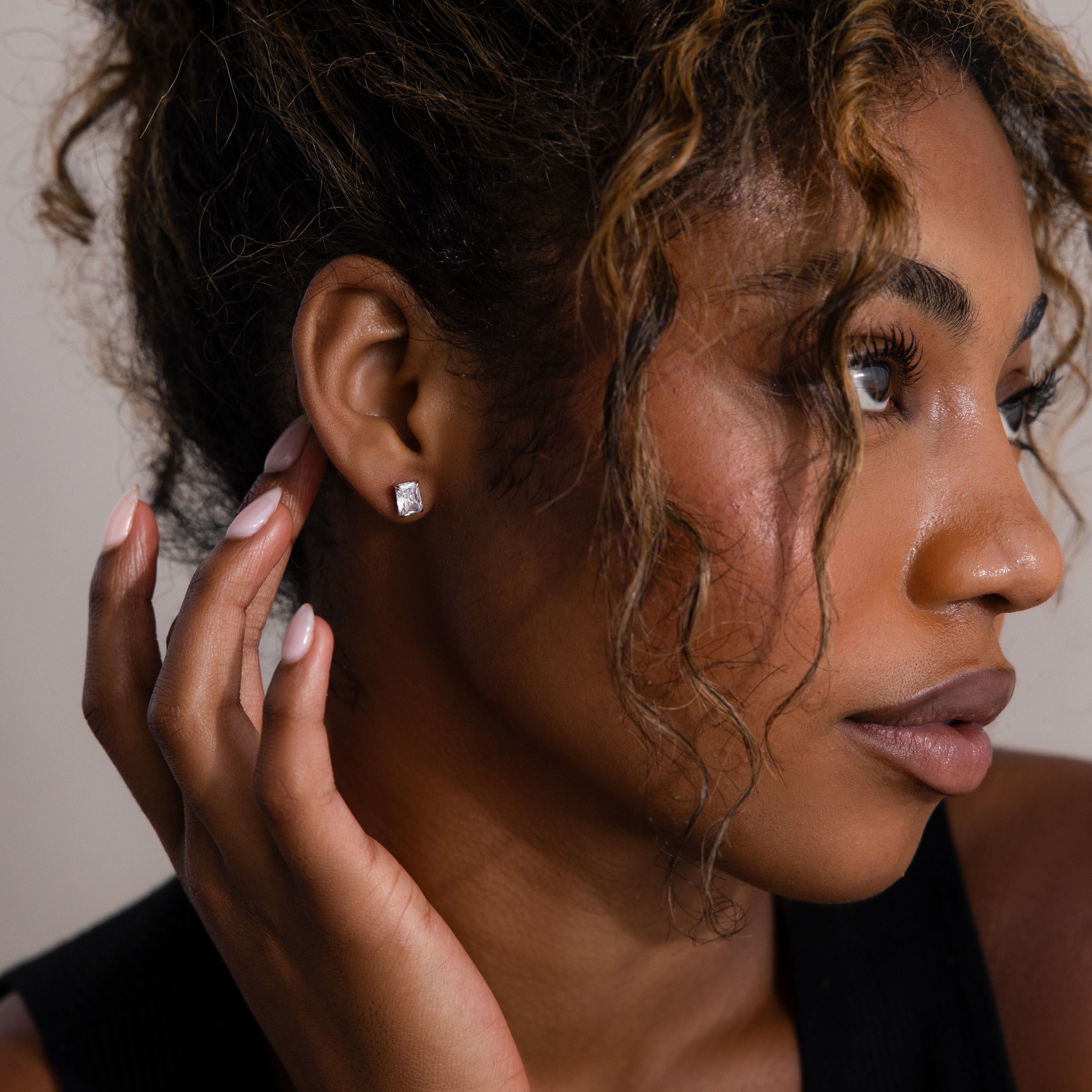 Woman adjusting a silver diamond earring with a neutral background