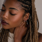 Woman with braided hair wearing a silver huggie hoop earring against a neutral background