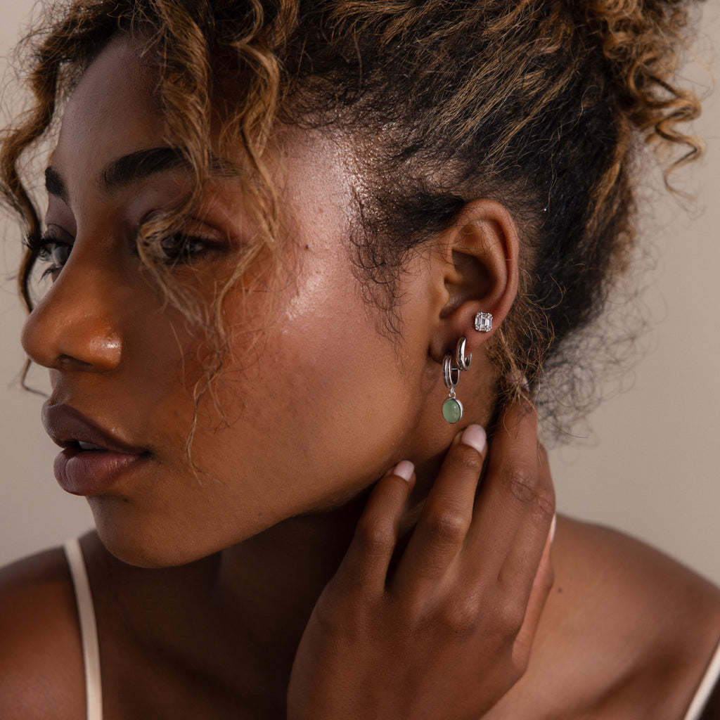 Woman wearing multiple silver earrings with a neutral background
