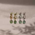 Two pairs of stud hoop earrings with green jade stones in gold and silver on a neutral background