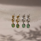 Two pairs of stud hoop earrings with green jade stones in gold and silver on a neutral background