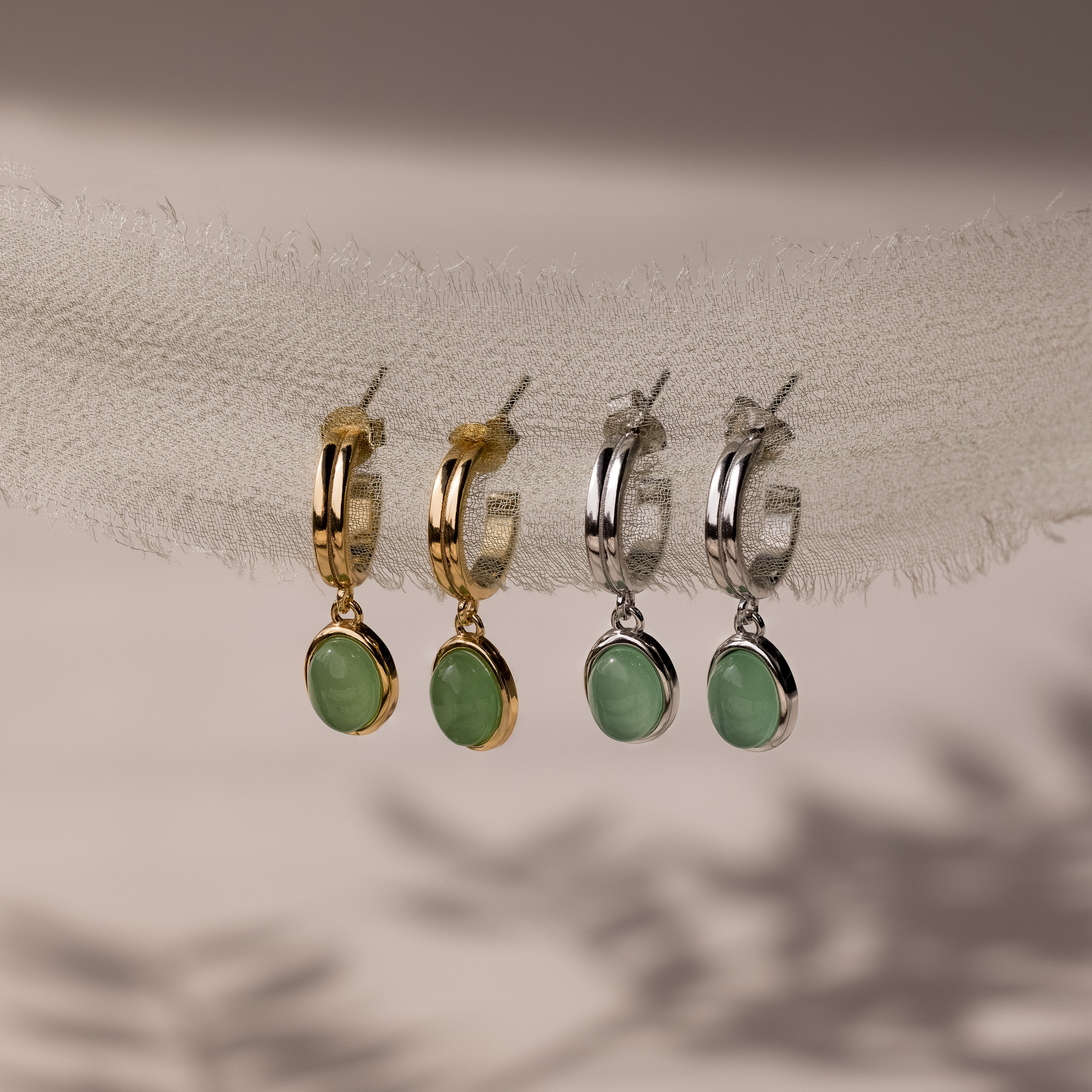 Two pairs of stud hoop earrings with green jade stones in gold and silver on a neutral background