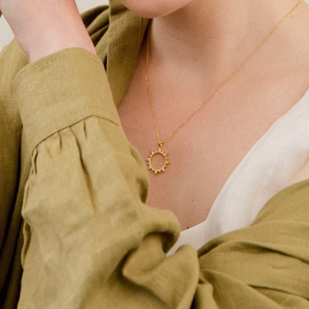 A woman in an olive green blouse wears the Pave Sun Necklace, featuring sparkling pave accents.