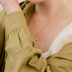A woman in an olive green blouse wears the Pave Sun Necklace, featuring sparkling pave accents.