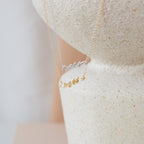 The Mrs. Necklace in silver and gold rests on a textured, light surface—an elegant wedding gift for any bride-to-be.