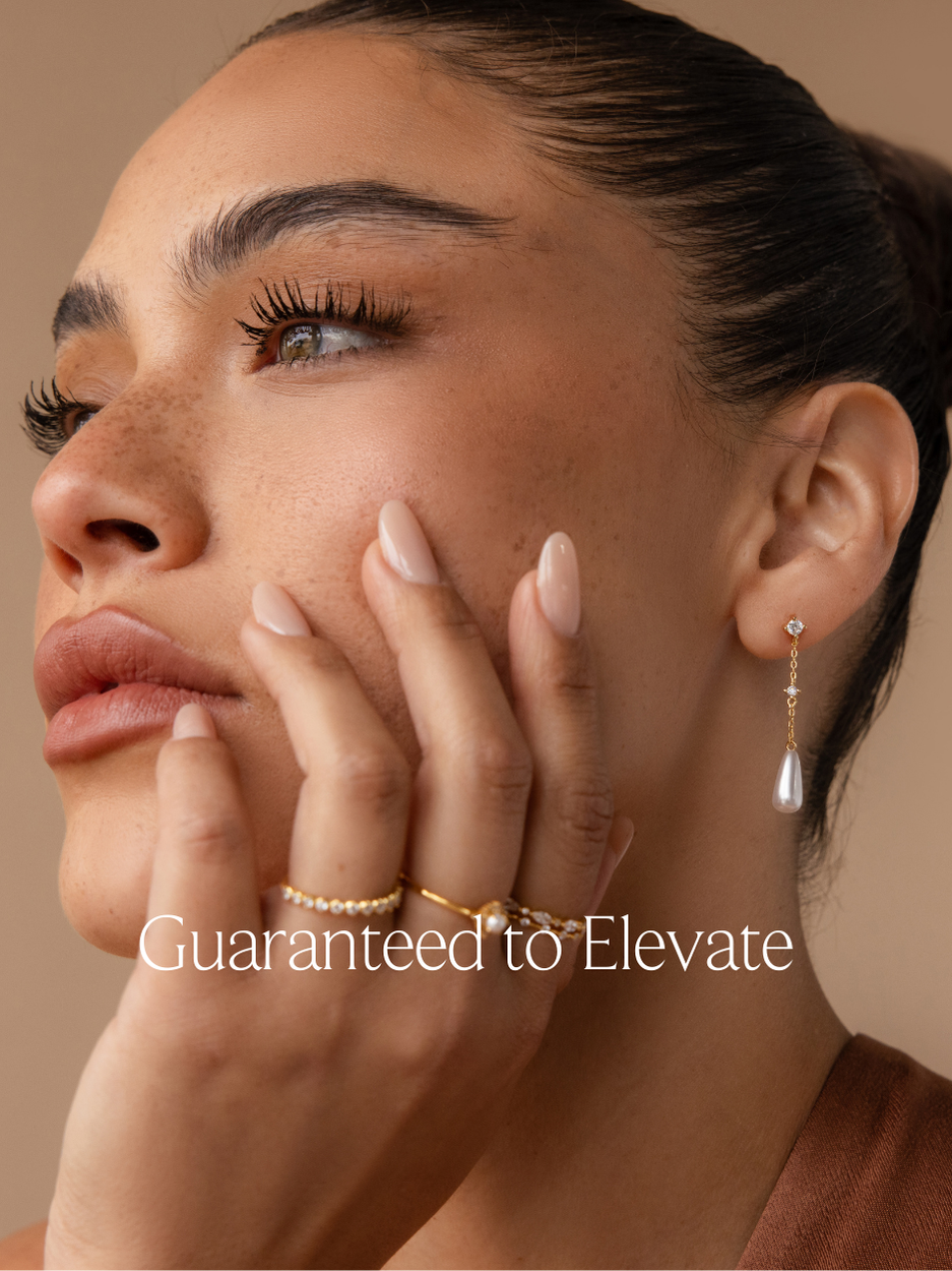 A banner with text "guaranteed to elevate" featuring a jewelry model photo of a gold jewelry stack consisting of a diamond and pearl chain drop earring, 1 diamond ring, 1 pearl ring and a diamond ring set.