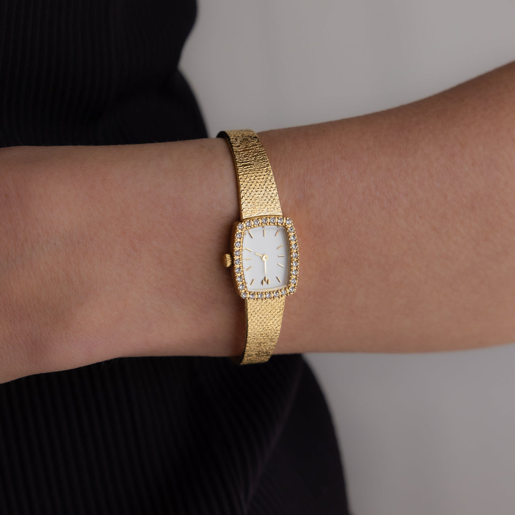 A Petite Mesh Timepiece with a gold rectangular face and gemstone accents adds elegance to any wrist.