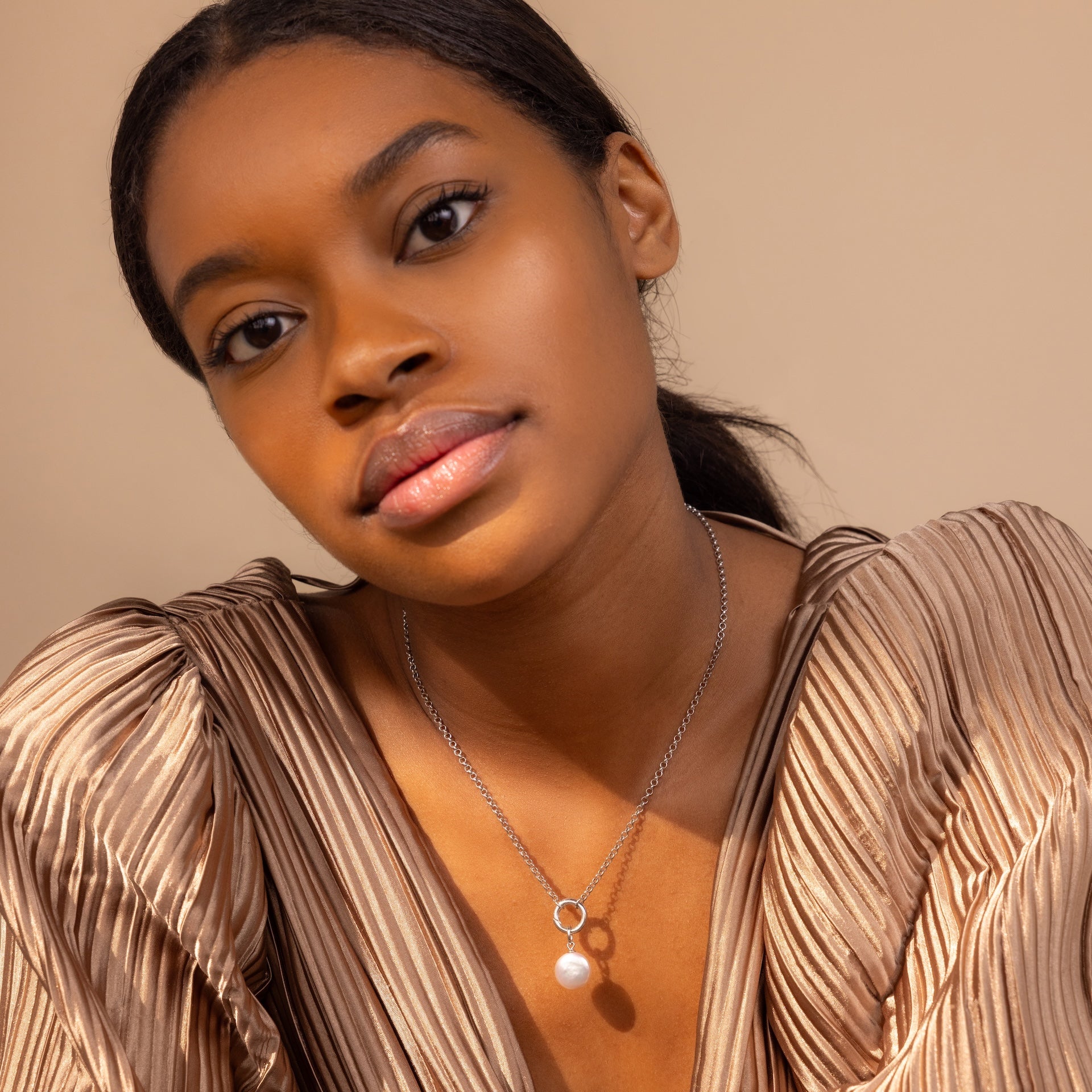 Woman in a pleated beige top wears a silver necklace featuring the Round Pearl Charm and a Mother of Pearl pendant against a neutral background.