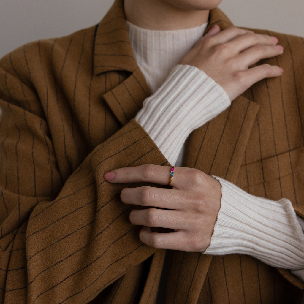 A person in a brown pinstripe coat and white sweater is wearing the Toi et Moi Tapered Birthstone Ring on their finger.
