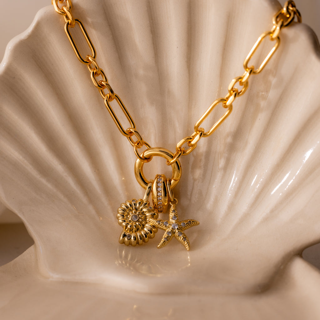 The Pave Dome Charm adds sparkle to your jewelry stack, shown here on a gold chain necklace and displayed on a cream-colored ceramic shell.