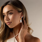 Woman with long hair touches her ear while wearing Celestial Baroque Pearl Charm Hoops and a cream halter top.