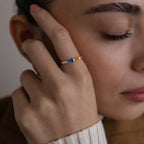 A person touches their face, showcasing the Toi et Moi Tapered Birthstone Ring featuring striking blue and yellow accents on their finger.