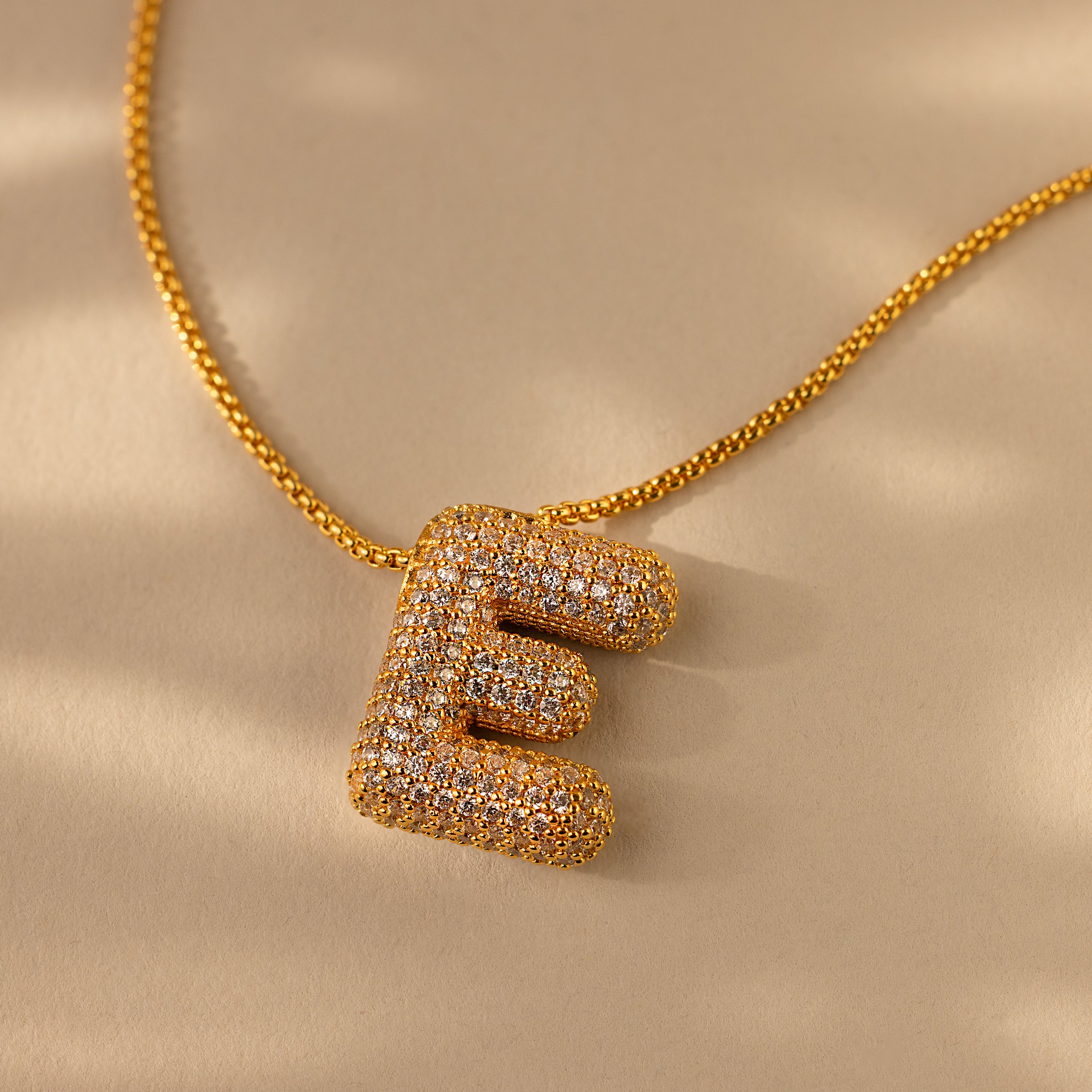Pave Puff Letter Necklace in 18K Gold featuring a pavé diamonds-encrusted letter E pendant, shown on a beige background.
