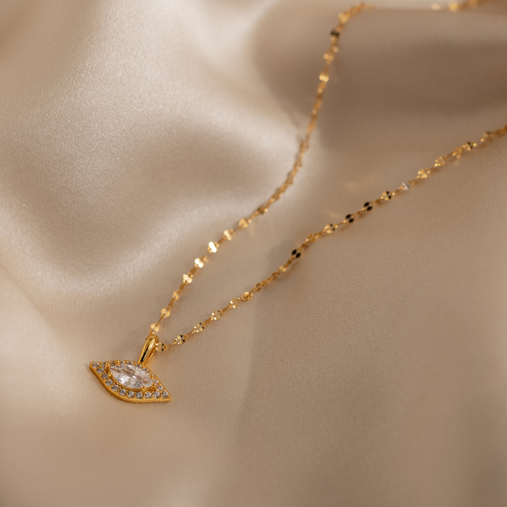 Gold Pave Evil Eye Charm on a mirror chain laying on fabric