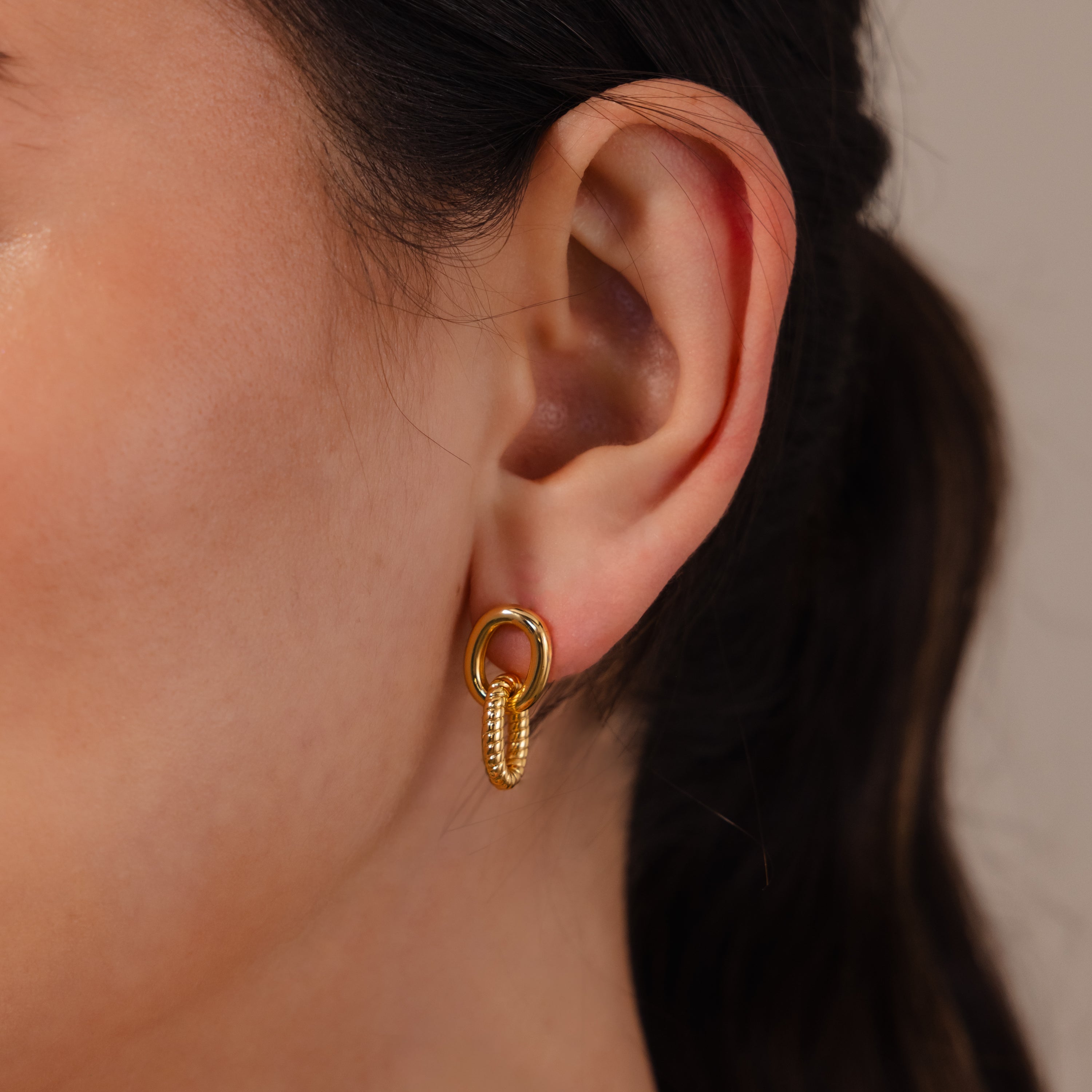 Close-up of a woman's ear wearing Twisted Link Earrings, featuring gold hoops with a textured design for a modern, stylish look.