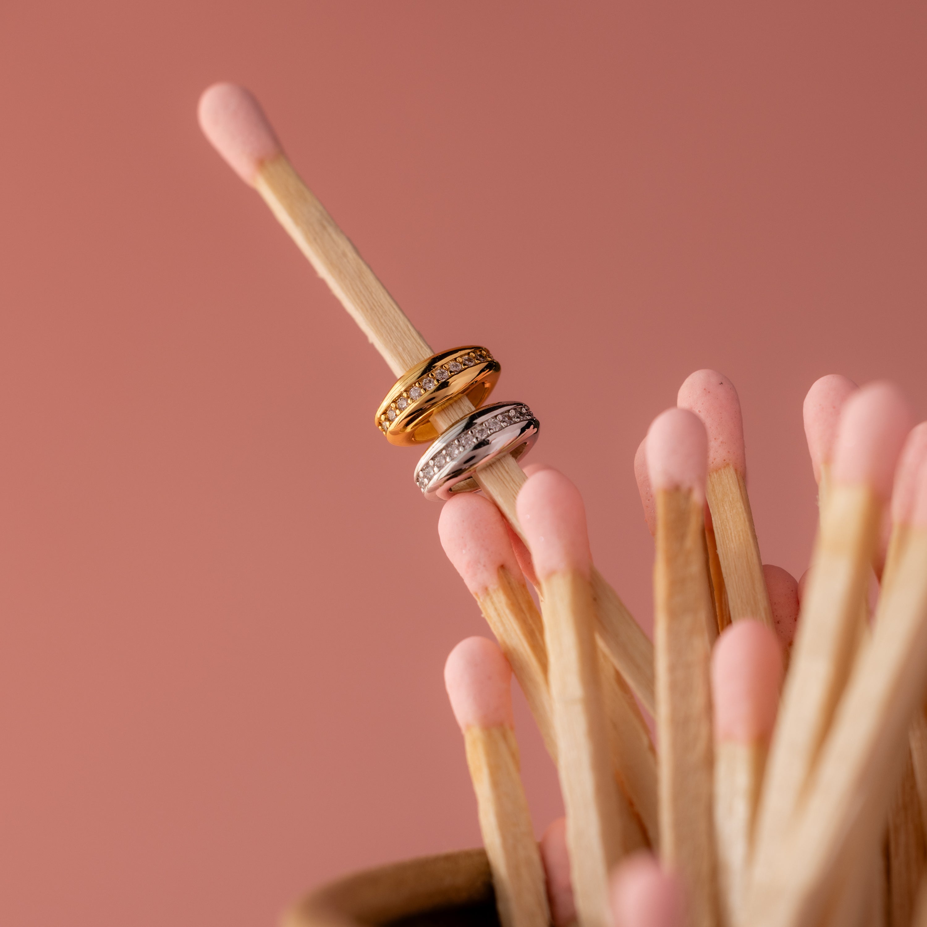 The Pave Dome Charm in Silver is stacked on the tip of a matchstick among pink-tipped matches, adding a hint of sparkle and subtle charm to the playful scene.