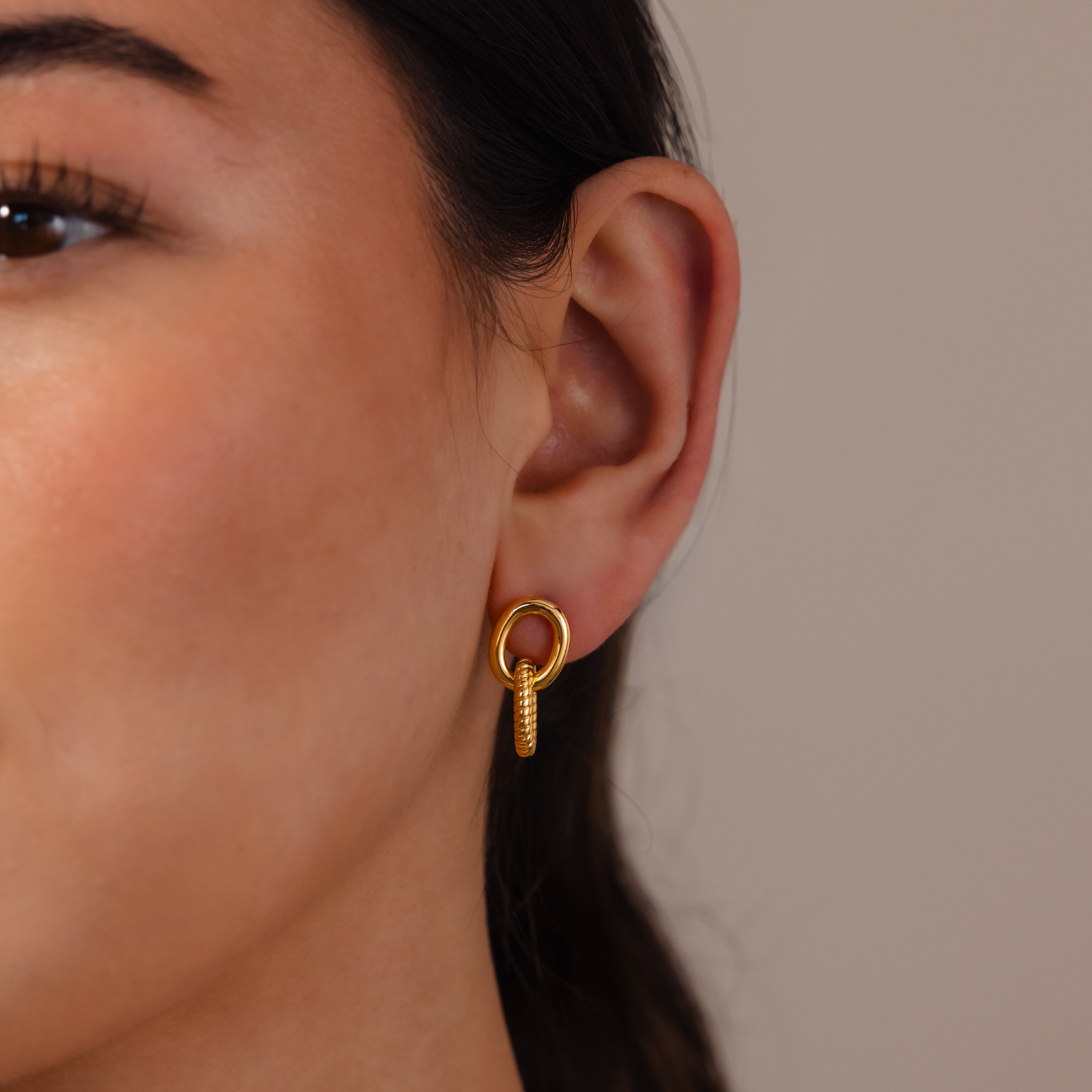 Close-up of a woman's ear wearing Twisted Link Earrings in 18K Gold—modern hoops with a textured, vertical design—for an elegant jewelry statement.
