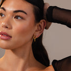 Woman with smooth skin wears Twisted Link Earrings in 18K Gold and a sheer black sleeve, gazing off to the side.