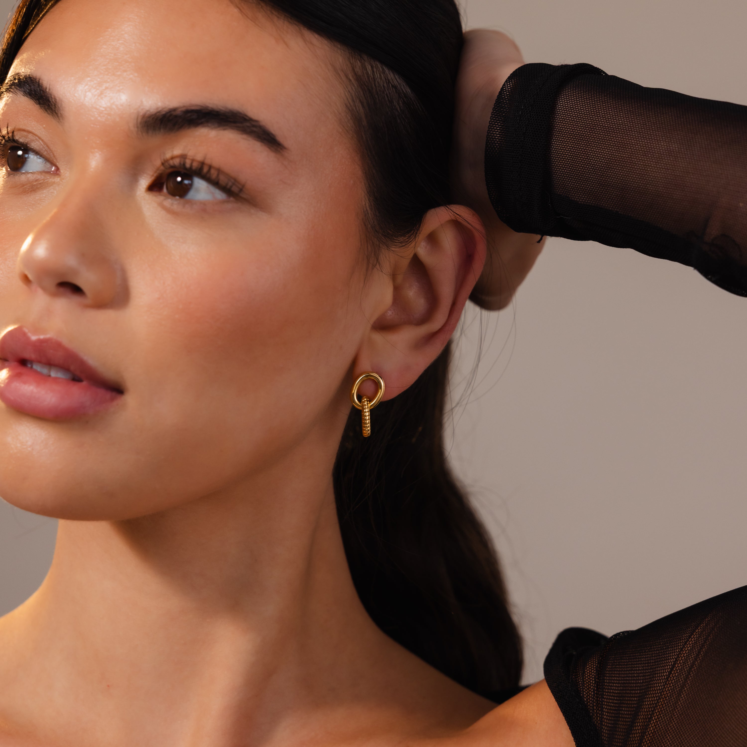 Woman with smooth skin wears Twisted Link Earrings in 18K Gold and a sheer black sleeve, gazing off to the side.