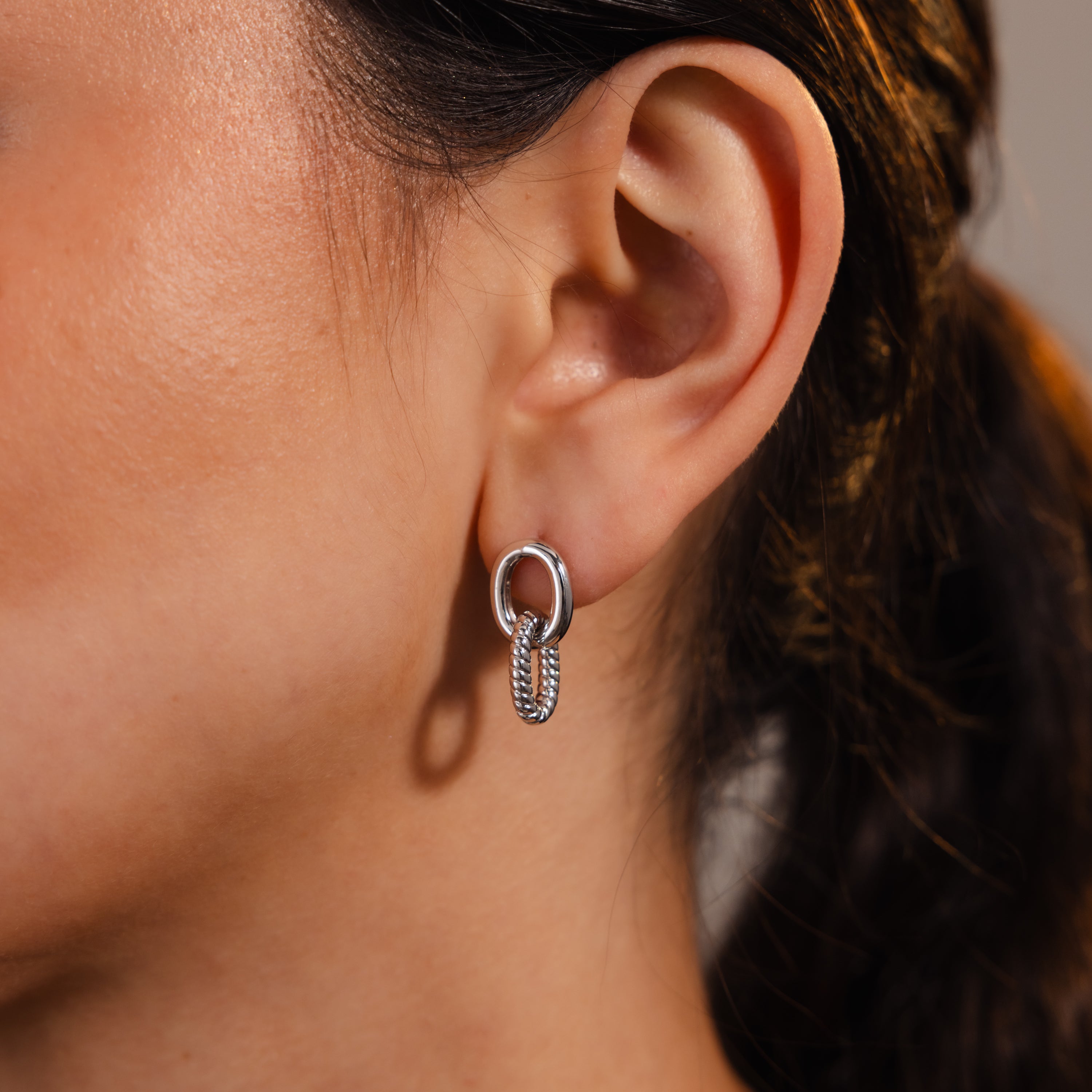 Close-up of a woman’s ear wearing Twisted Link Earrings in White Gold—these modern earrings feature a unique design that adds timeless elegance to any look.