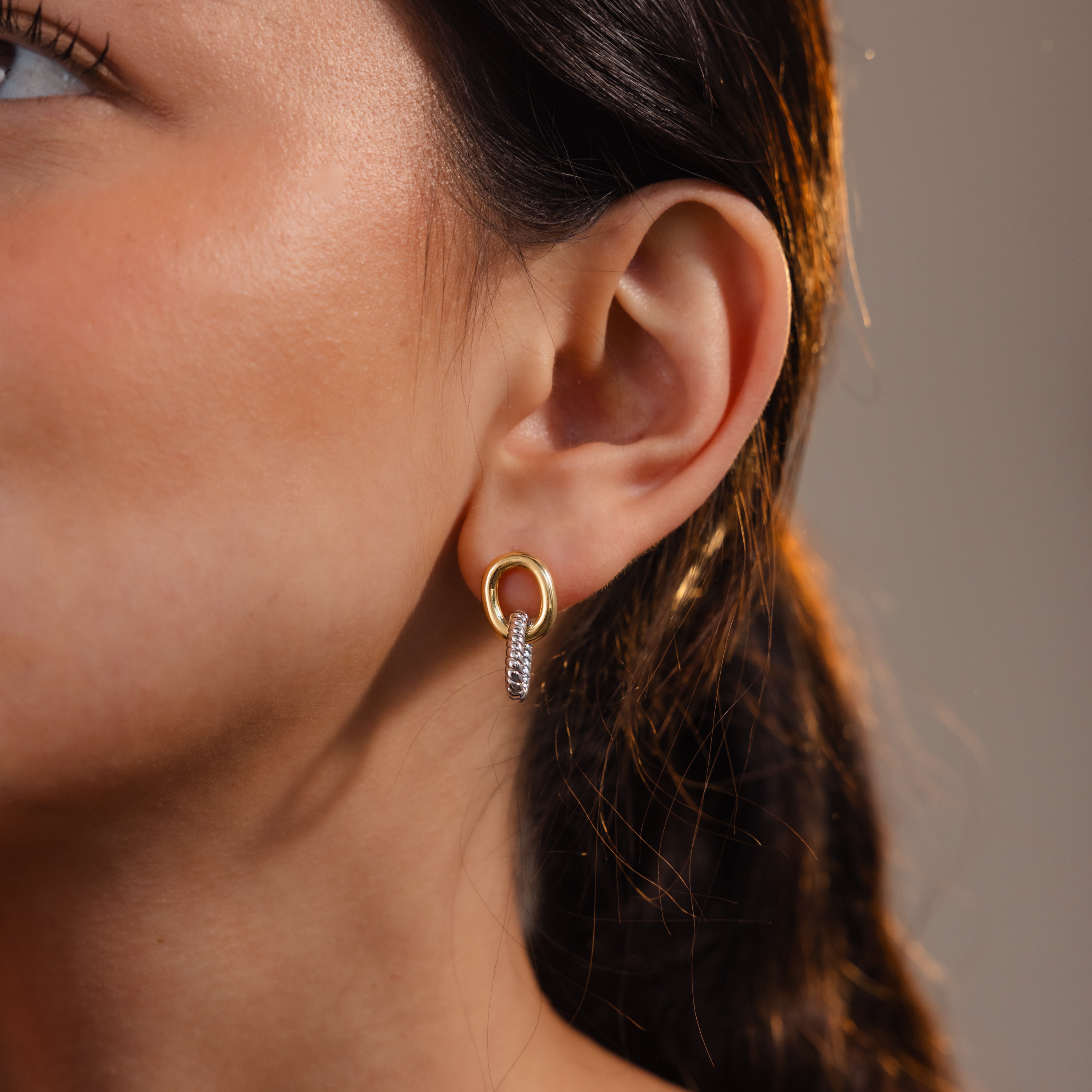 Close-up of a woman's ear wearing Twisted Link Earrings in Mixed Metal—a gold and silver hoop with a dangling, sculptural design.