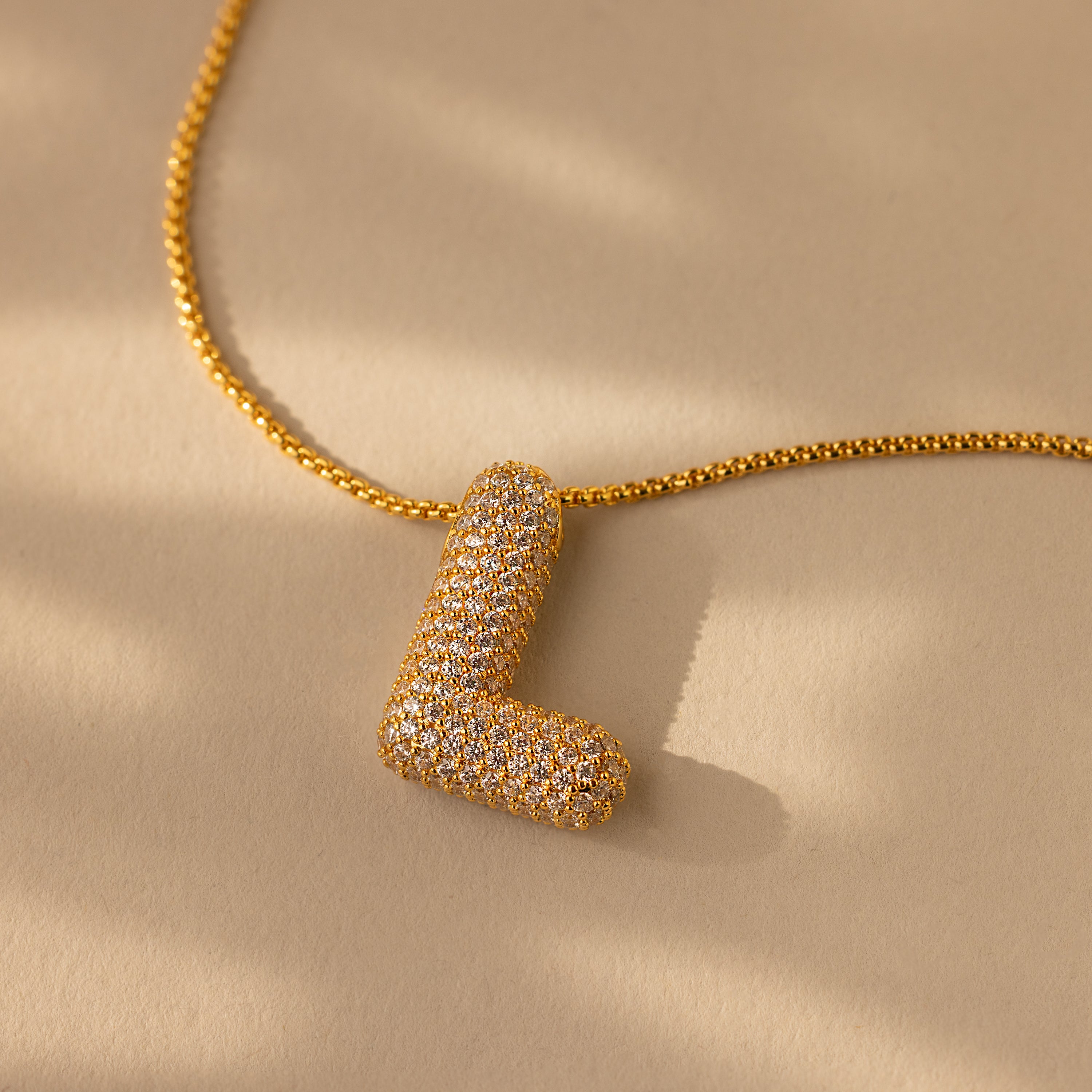 Pave Puff Letter Necklace in 18K Gold featuring a diamond-encrusted L-shaped charm, elegantly showcased on a beige background.