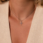 A woman wearing a knitted cream top and the Vintage Diamond Cross Necklace in Silver, its jeweled cross pendant shining elegantly.