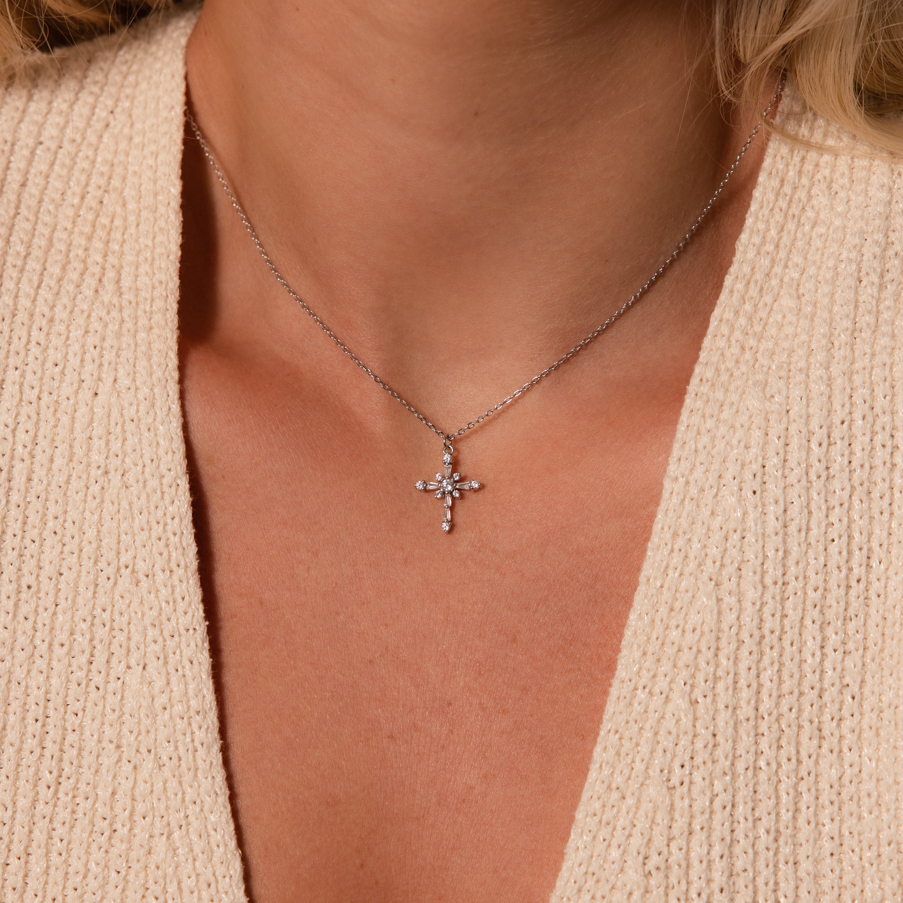 A woman wearing a knitted cream top and the Vintage Diamond Cross Necklace in Silver, its jeweled cross pendant shining elegantly.