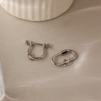 The Bar & Carabiner Charm Set features two silver ear cuffs with geometric designs on a beige surface—ideal as charm connectors or for pairing with favorite necklace accessories.