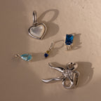 Several different silver charms including the dainty duo birthstone charm, teardrop birthstone charm, emerald birthstone charm, bow charm and pearl heart charm