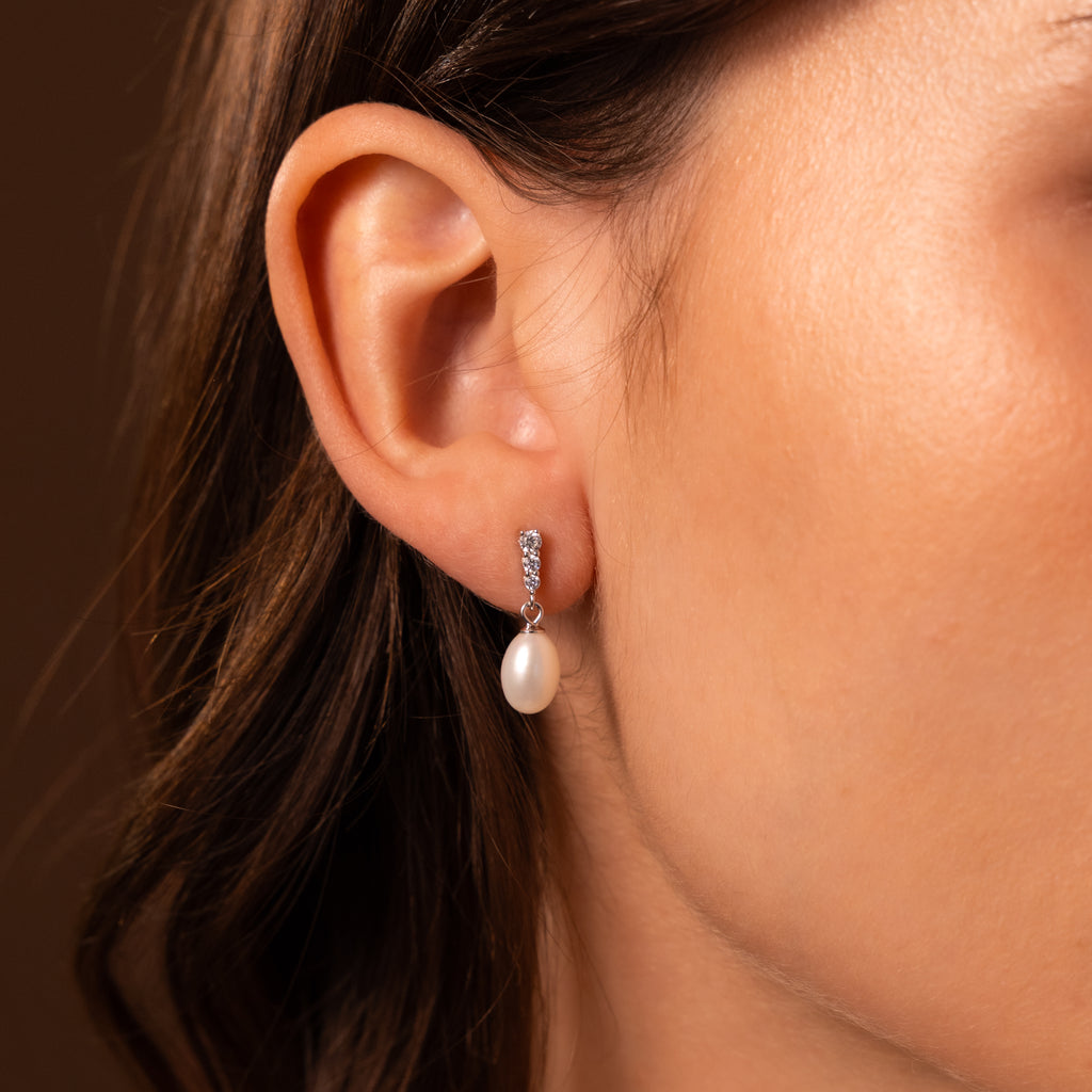 Close-up of a woman's ear wearing Diamond Pearl Droplet Earrings in Sterling Silver, featuring small sparkling stones and an elegant dangling pearl.