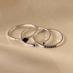 Three delicate silver bands from the Black Abyss Ring Set in Silver, each with a small black gemstone, displayed on a soft beige fabric background.