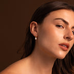 A woman with long brown hair wears Diamond Pearl Droplet Earrings in 18K Gold, posing against a brown background.