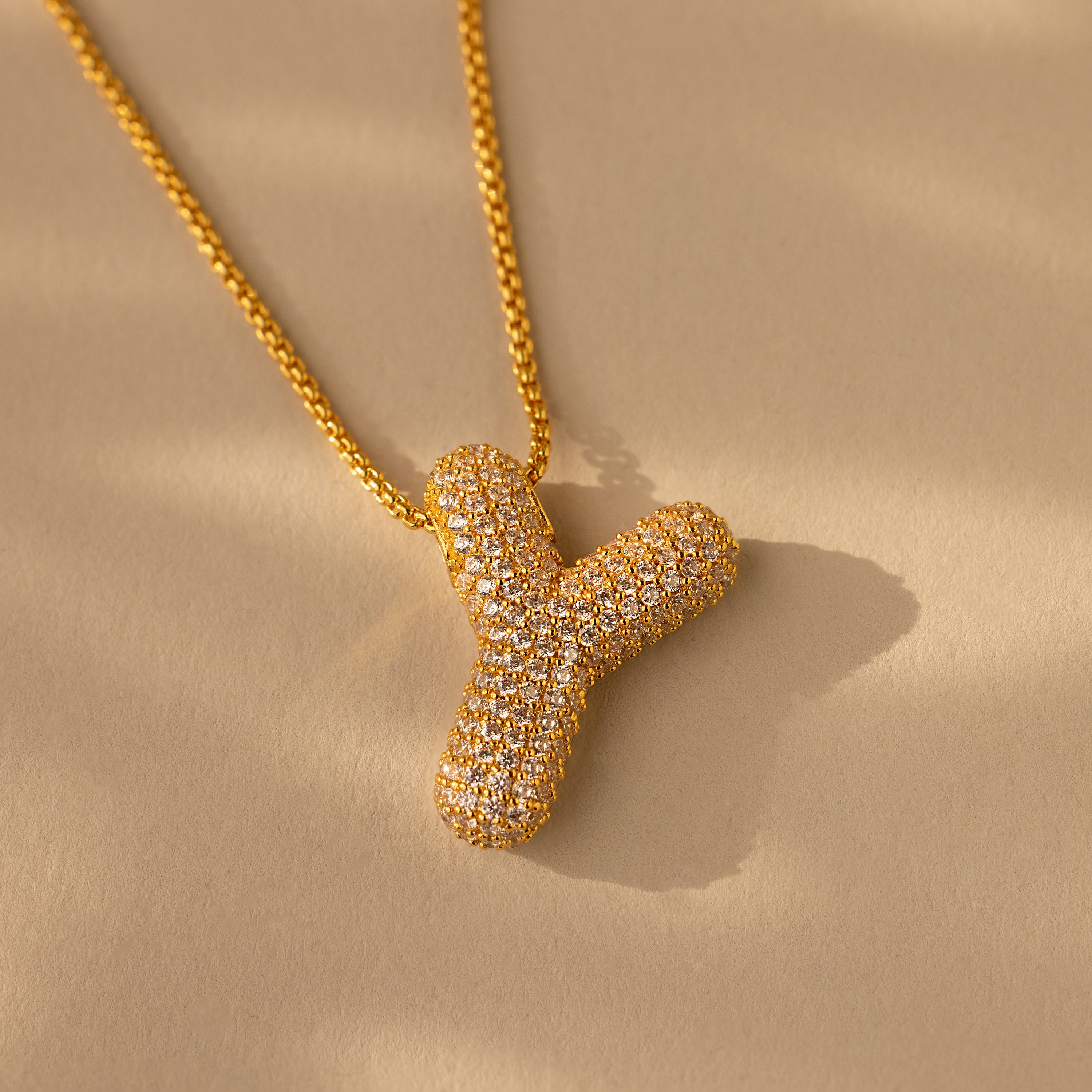 The Pave Puff Letter Necklace in 18K Gold features a sparkling, diamond-studded letter Y pendant displayed on a beige background.