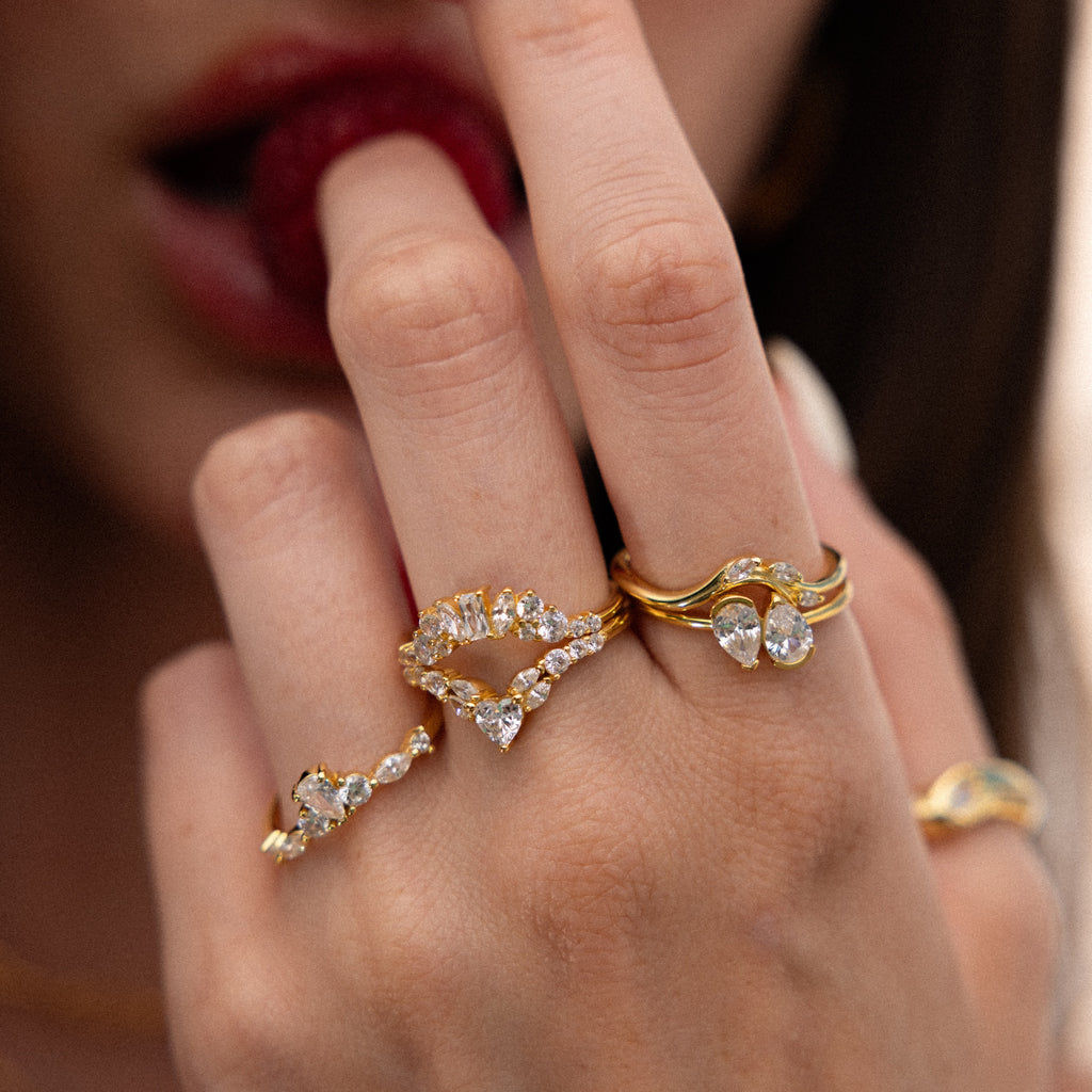 A hand wears the Toi et Moi Pear Birthstone Ring with diamond bands, held near lips; the softly blurred face in the background creates a sense of mystery around this romantic gift.