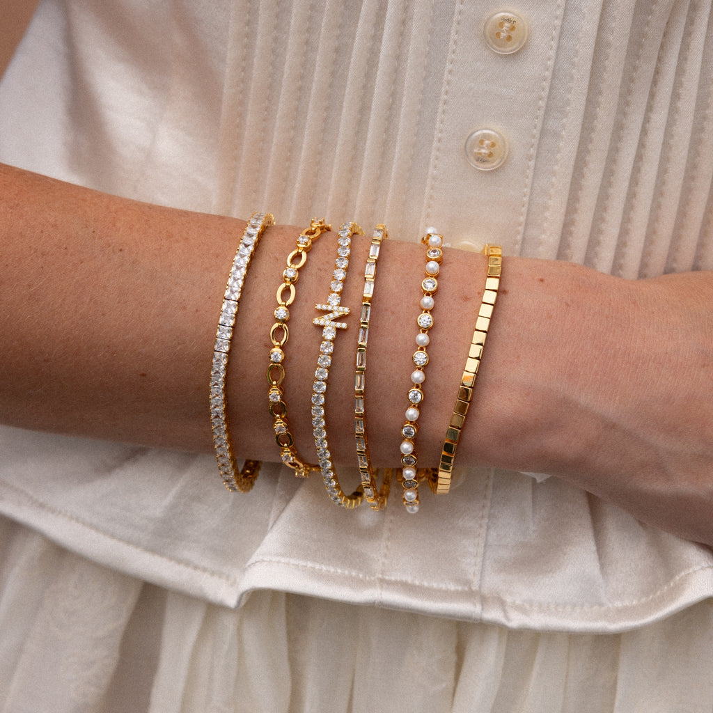 A person in a white top showcases six Pearl  Diamond Tennis Bracelets, stylishly stacked on their wrist.