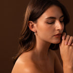 A woman with closed eyes and clasped hands, looking thoughtful, wears glowing Round Pearl Hoops in Sterling Silver against a brown background.