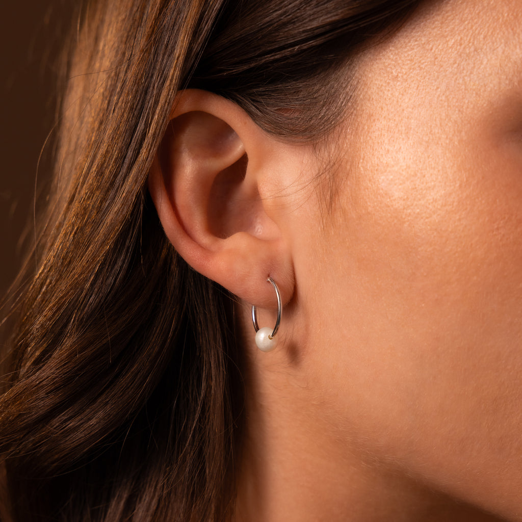 Close-up of a woman's ear wearing the Round Pearl Hoops in Sterling Silver, featuring polished hoops with a glowing pearl charm that adds subtle elegance to her look.
