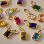 Multiple emerald-cut birthstone charms in different colors arranged side-by-side. Ruby and Sapphire charms are at the center