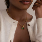 Woman wearing a gold rolo chain with several green emerald charms