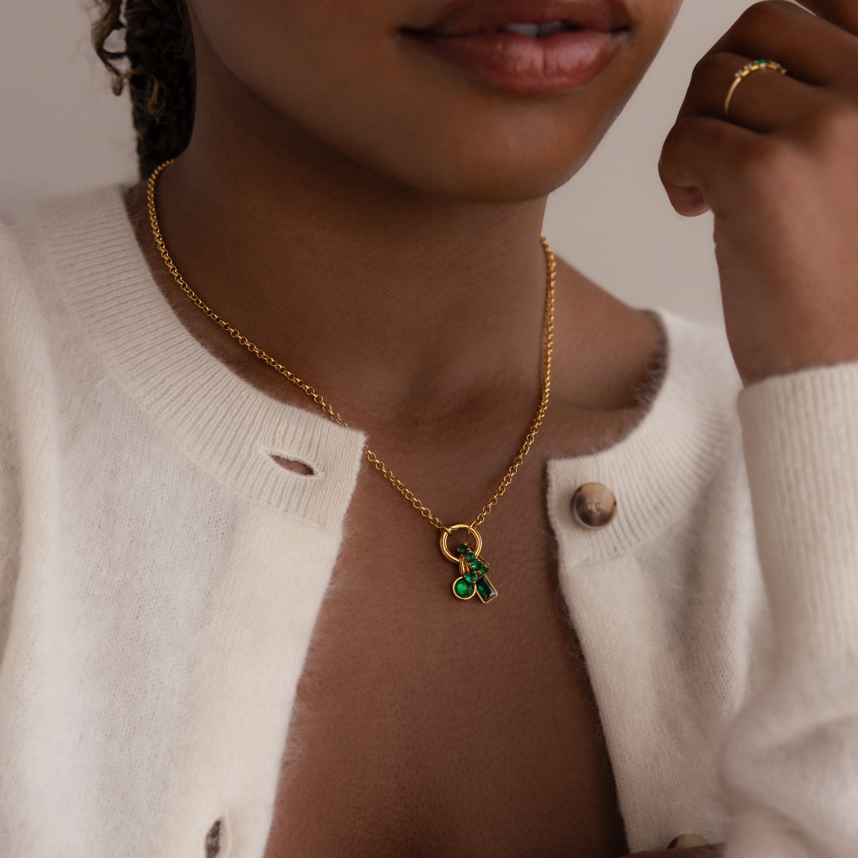Woman wearing a gold rolo chain with several green emerald charms