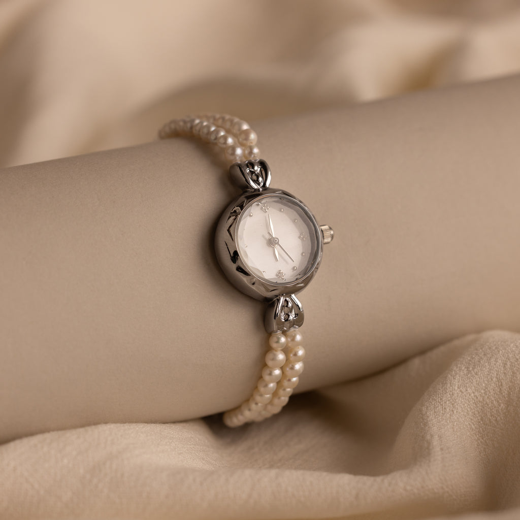 The Beaded Pearl Timepiece in Sterling Silver adorns a model's wrist, elegantly displayed against a beige fabric backdrop.