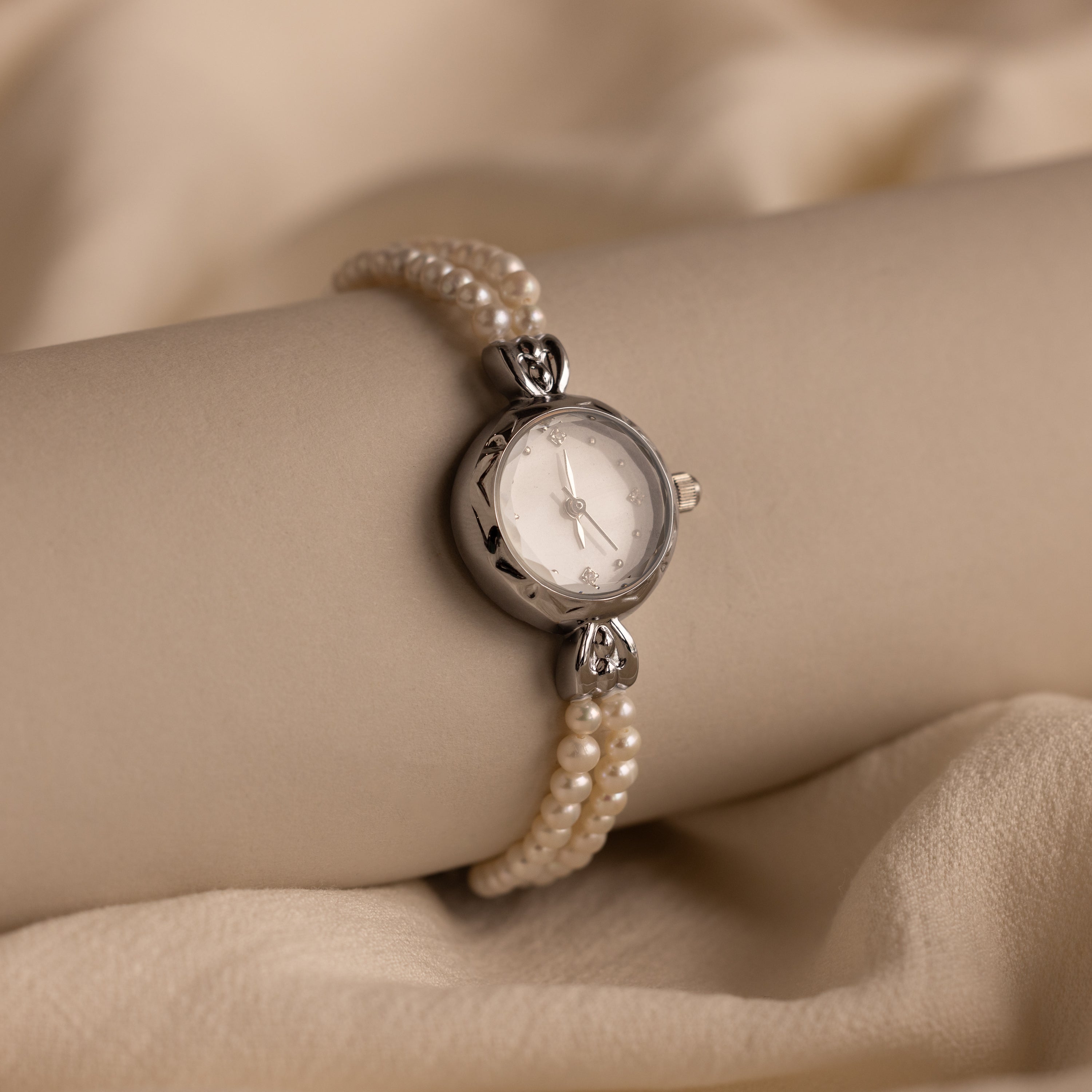 The Beaded Pearl Timepiece in Sterling Silver adorns a model's wrist, elegantly displayed against a beige fabric backdrop.