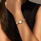 A woman in a sleeveless black top raises her hand to her face, showcasing the Beaded Pearl Timepiece on her wrist.