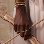 A hand wearing the Ribbed Heart Link Bracelet holds wooden objects against a soft beige background, showcasing the bracelet’s vintage elegance and romantic style.