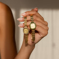 A manicured hand holds two elegant Pave Blossom Timepieces—gold womens watches with jeweled bezels—set against a neutral background.