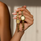 A manicured hand holds two elegant Pave Blossom Timepieces—gold womens watches with jeweled bezels—set against a neutral background.
