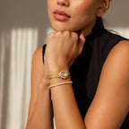 A woman in a sleeveless black top, wearing an elegant bracelet, rests her chin on her hands as the Pave Heart Timepiece sparkles with heart-shaped gemstones.