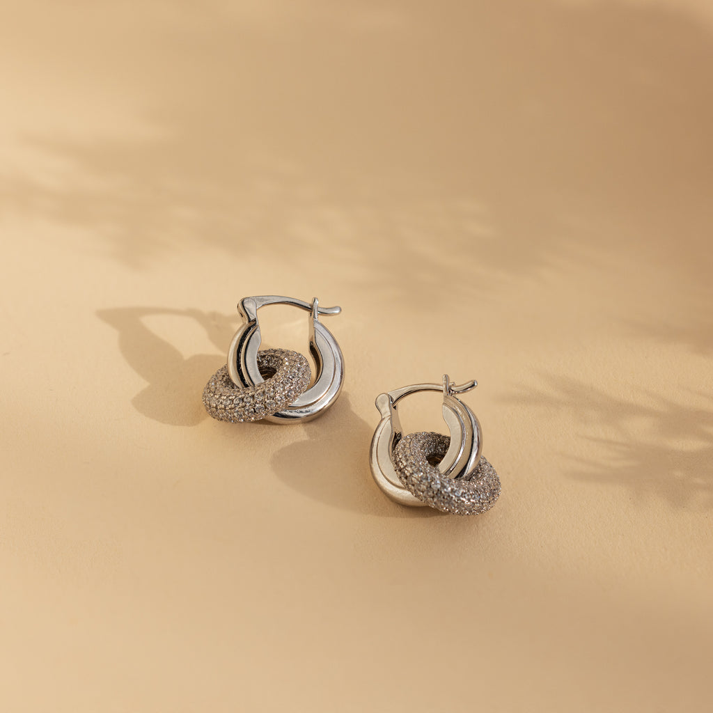 Duo Pave Link Hoops in White Gold, featuring intertwined textured and smooth rings, showcased on a beige background.
